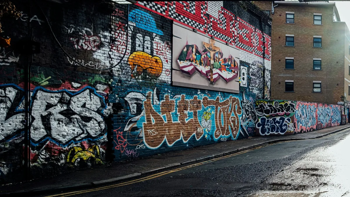 Lang murvegg dekket av graffiti og malerier langs en våt gate i East London