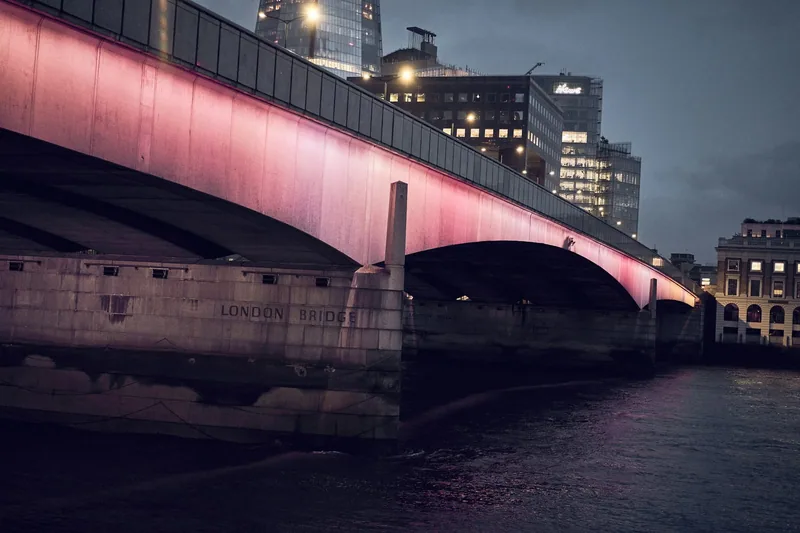 London Bridge opplyst i rosa om kvelden, med navnet hugget inn i brokaret ved elvekanten