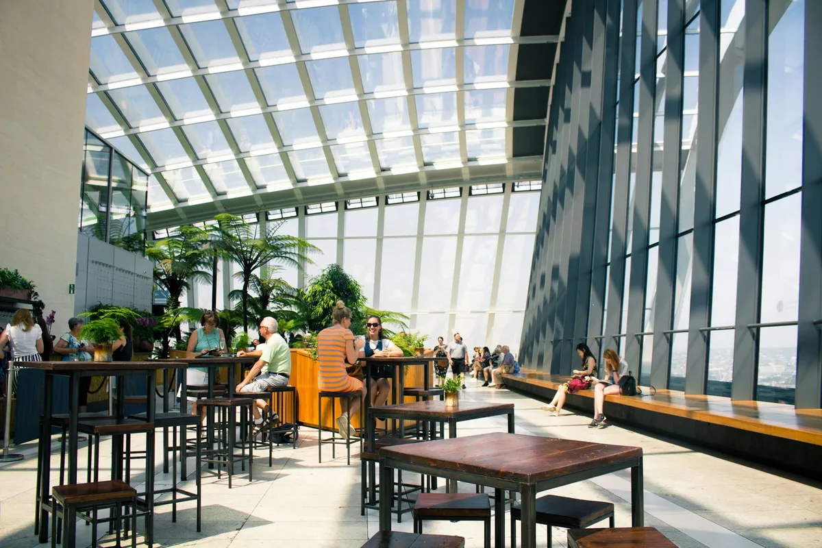 Besøkende ved barbord under glasstaket i Sky Garden, med bregnetrær og høye vinduer mot byen