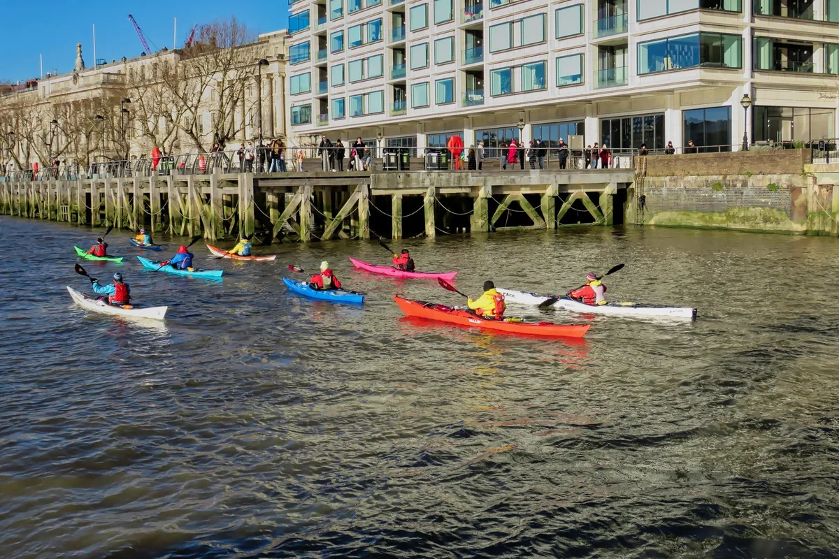 Padlere i fargerike havkajakker på Themsen ved en gammel trebrygge i City of London en solrik dag