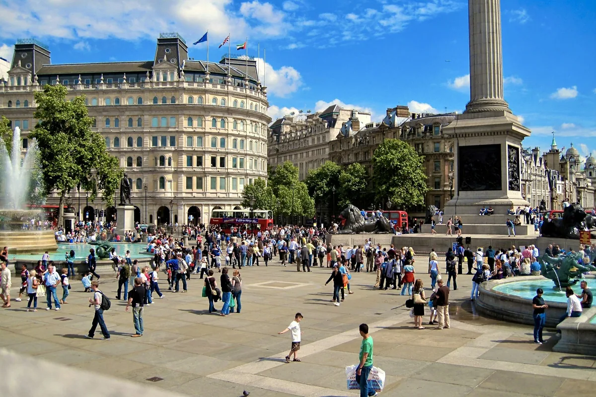 Trafalgar Square en solfylt dag med fontene, løvestatuer og sokkelen til Nelsonsøylen, full av besøkende