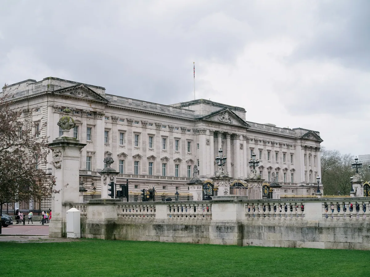 Østfasaden på Buckingham Palace med flagg på taket, sett over steinbalustraden en overskyet vårdag