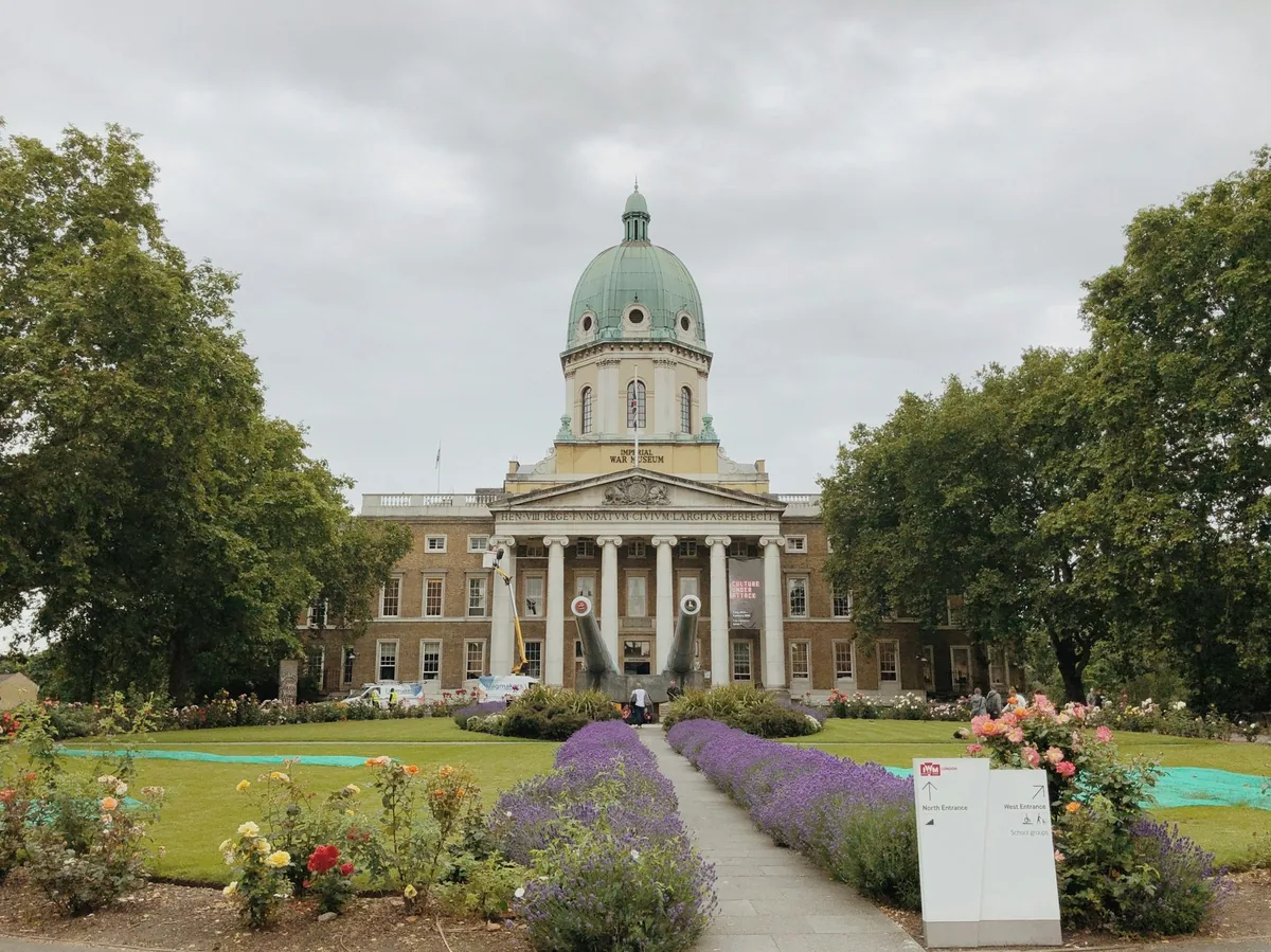 Imperial War Museum med grønn kobberkuppel og søylegang, sett fra hagen med lavendelbed og roser
