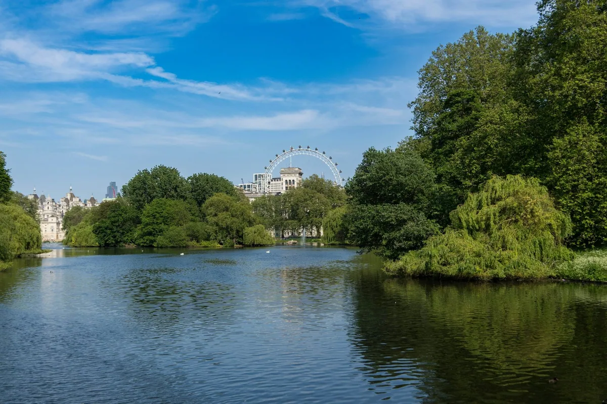 Innsjøen i St James's Park med Horse Guards og London Eye bak grønne trær en solrik dag