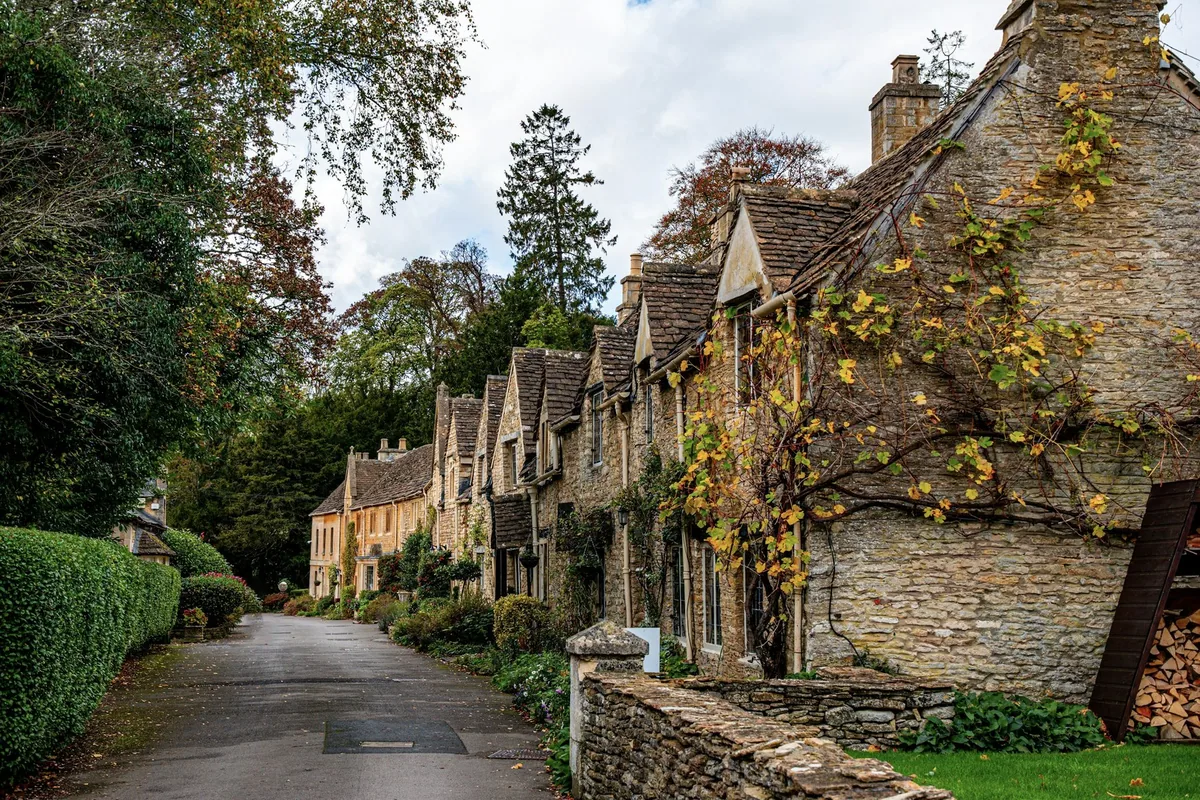 Rekke av gamle steinhus i gulbrun kalkstein langs en stille gate i Castle Combe i Cotswolds om høsten