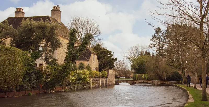 Elva Windrush med en lav steinbro og gamle hus i Bourton-on-the-Water i Cotswolds