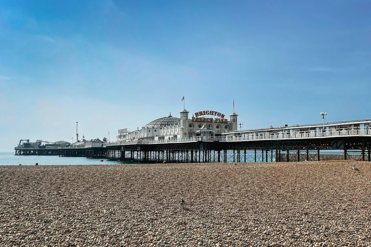 Brighton Palace Pier sett fra småsteinstranden under blå himmel