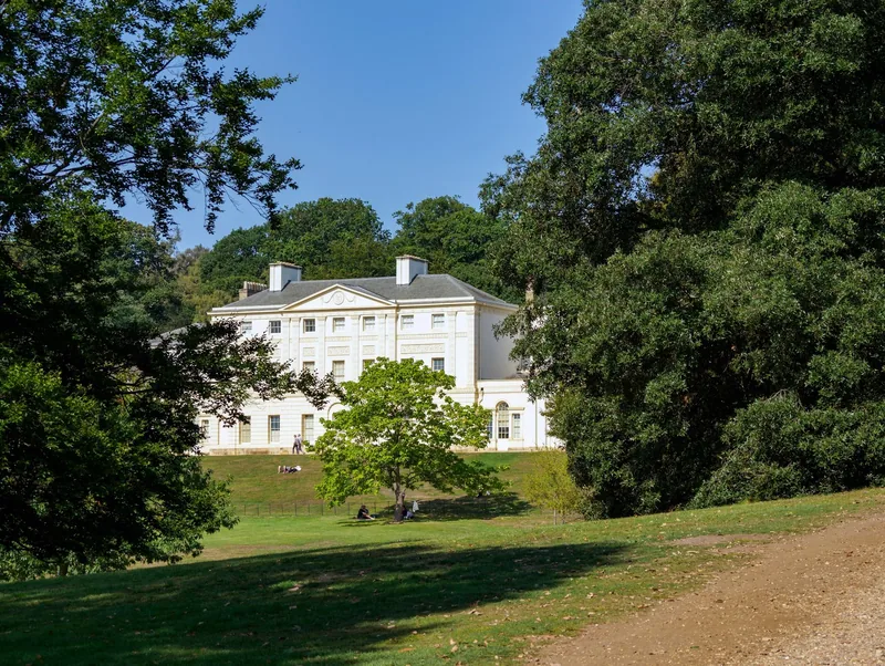 Det hvite herskapshuset Kenwood House på en gressbakke mellom store trær på Hampstead Heath