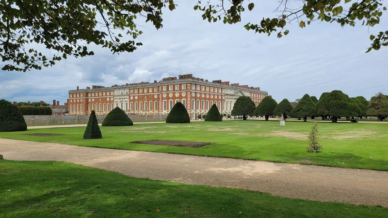 Barokkfløyen på Hampton Court Palace sett over plenene i hagen, med rader av formklipte barlind