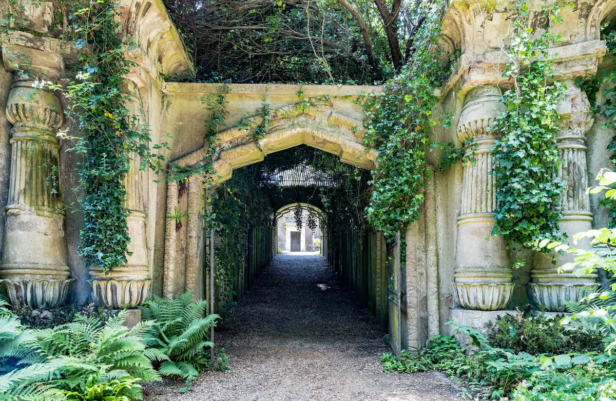 Inngangen til Egyptian Avenue på Highgate Cemetery med egyptiske søyler, eføy og bregner rundt porten