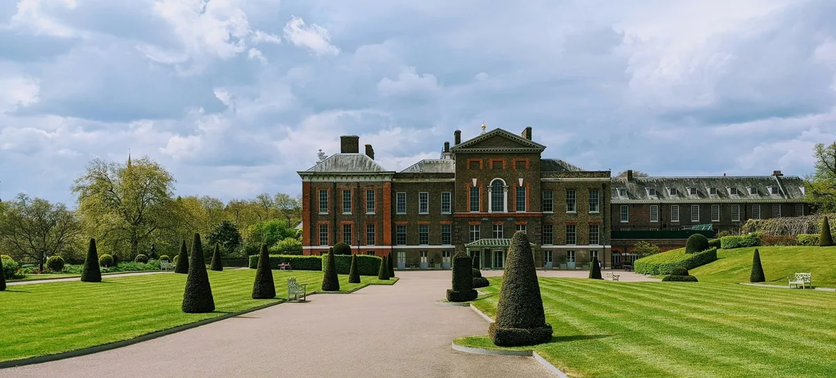 Kensington Palace i rød tegl sett langs en allé med formklipte trær og stripete plener