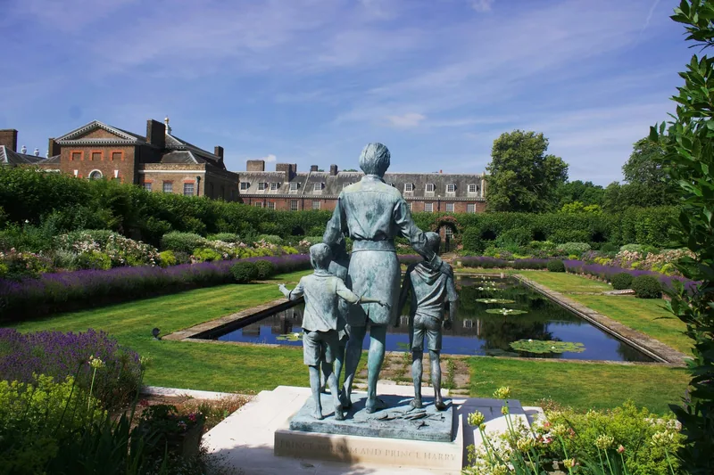 Minnestatuen av prinsesse Diana omgitt av barn i Sunken Garden, med dammen og slottet bak