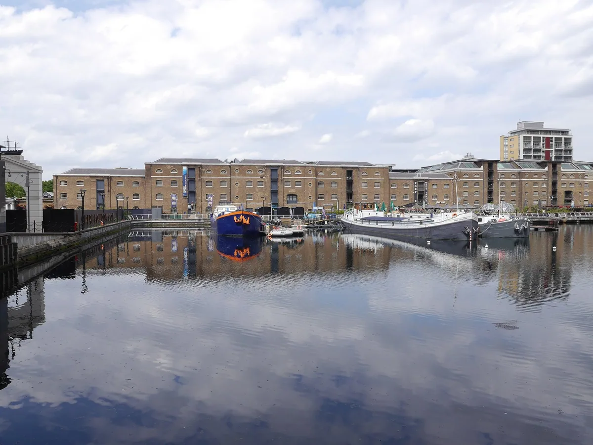 Rekken av gamle lagerbygninger i mursten ved West India Quay, der museet holder til, speilet i vannet i North Dock