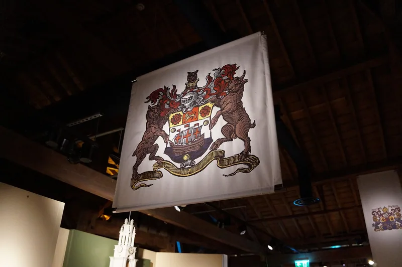 Et stort banner med våpenskjold og seilskip under de gamle takbjelkene i museet i Docklands