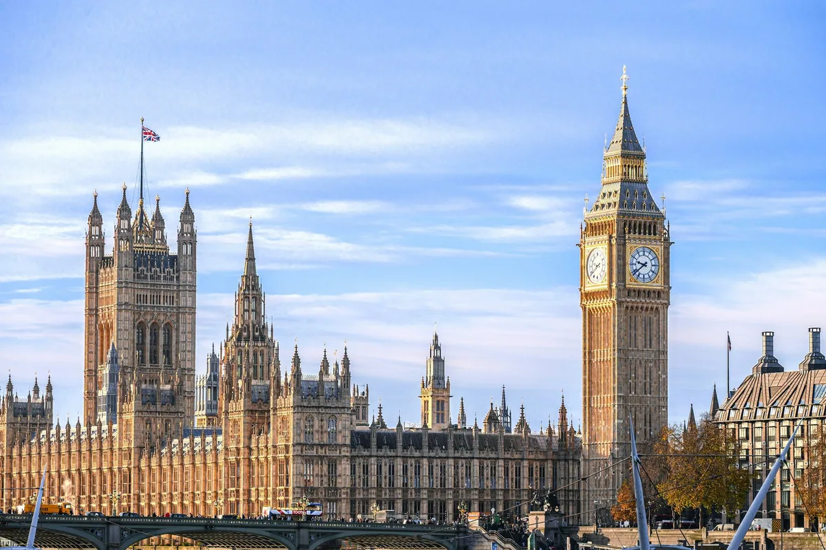 Parlamentsbygningen Palace of Westminster med Victoria Tower og Big Ben i lavt sollys bak Westminster Bridge