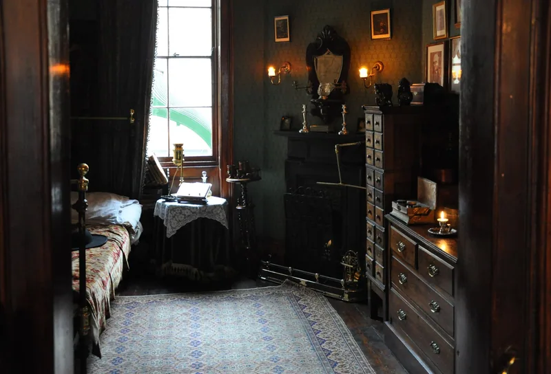 Doktor Watsons rom i Sherlock Holmes Museum med smal seng, kommode, levende lys og mønstret teppe