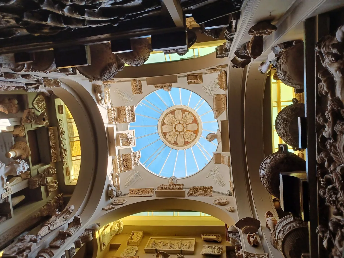 Takvindu med rosett sett nedenfra, omgitt av antikke skulpturfragmenter og urner i Sir John Soane's Museum