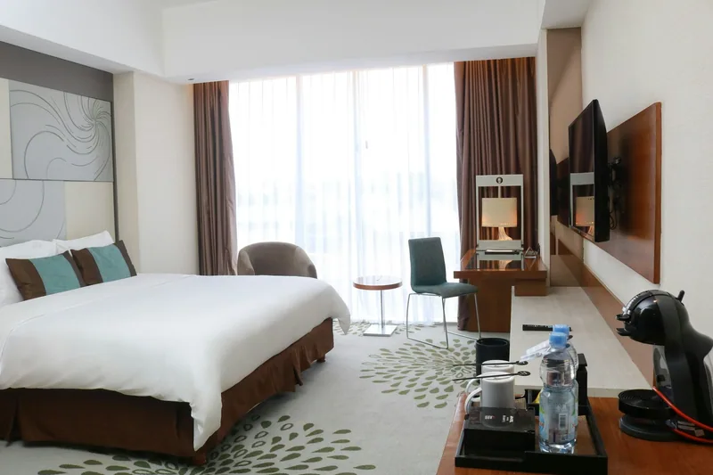 Enkelt hotellrom med dobbeltseng, lite skrivebord, veggmontert TV og kaffemaskin ved vinduet