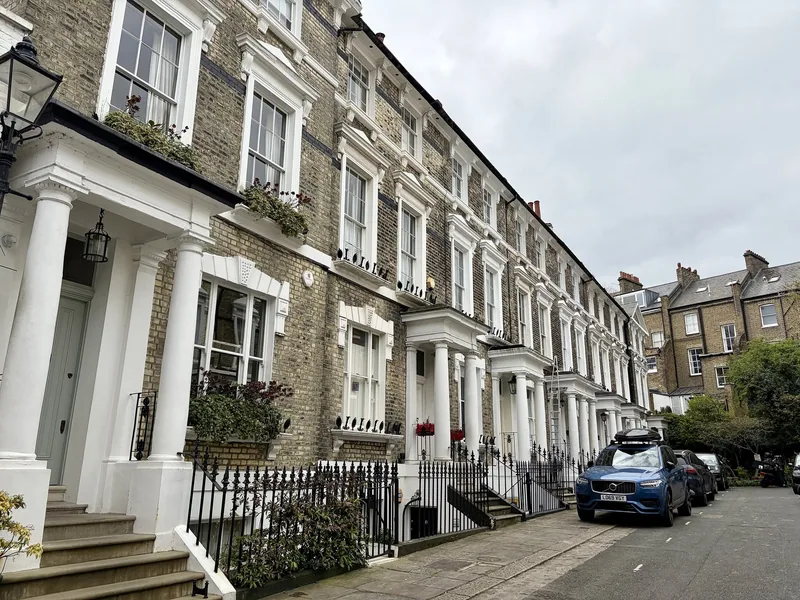 Rekke av lyse viktorianske rekkehus med søyler og smijernsgjerder i en rolig gate i Primrose Hill