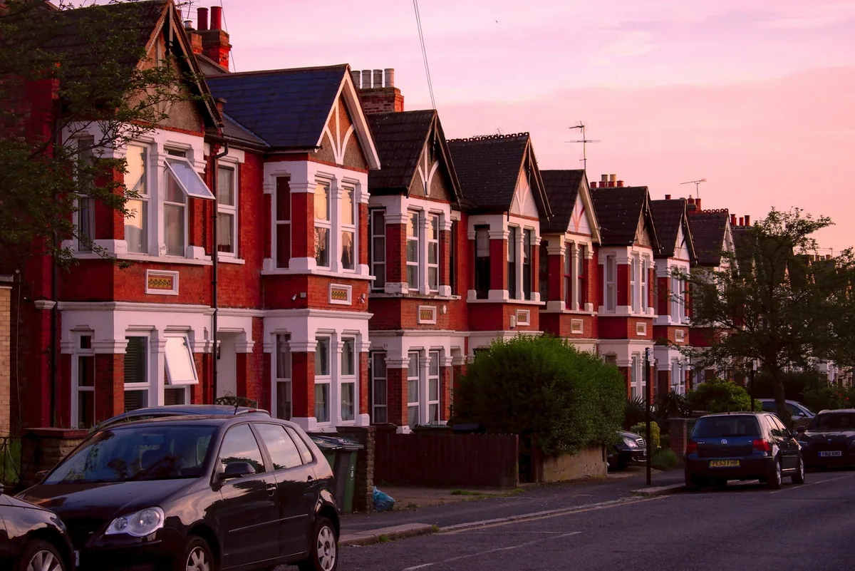 Rekke med viktorianske rekkehus i rød murstein i Leytonstone i London, med parkerte biler og rosa kveldshimmel