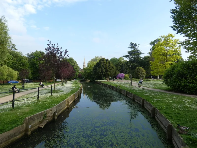 New River Loop i Enfield Town: en rett kanal mellom gressplener, med et kirkespir mellom trærne