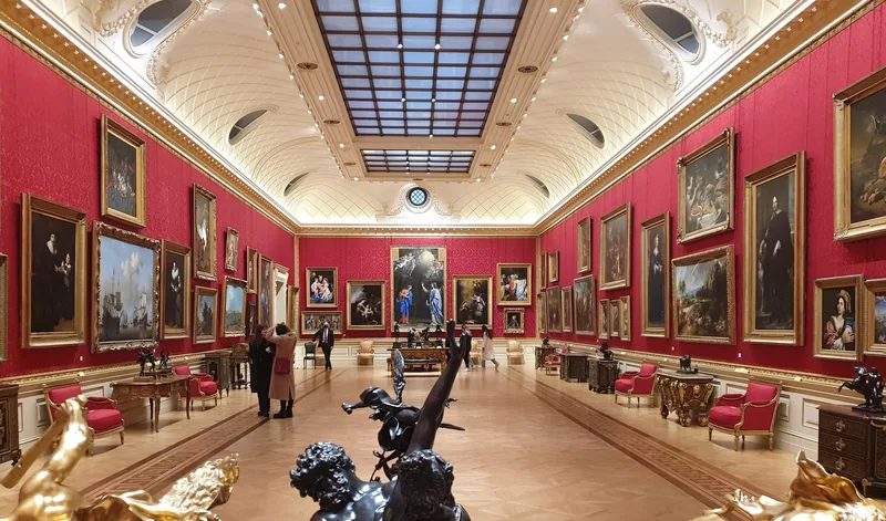 Et langt galleri i Wallace Collection med røde vegger, gullrammede malerier og overlys