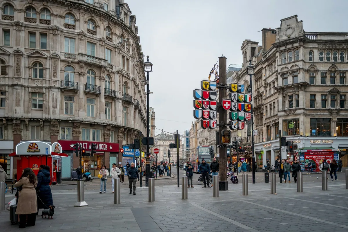 Den sveitsiske kantonstolpen med våpenskjold på Leicester Square, med fotgjengere og en rød buss i bakgrunnen