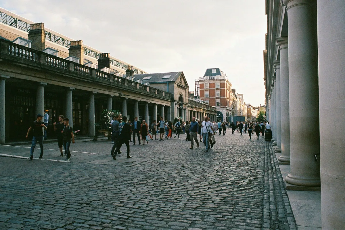 Folk som går over brosteinen ved søylegangene på Covent Garden en solrik ettermiddag