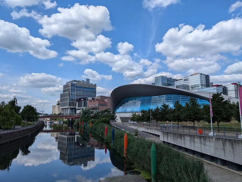 London Aquatics Centre med det bølgende taket ved kanalen i Olympiaparken, med nye kulturbygg bak