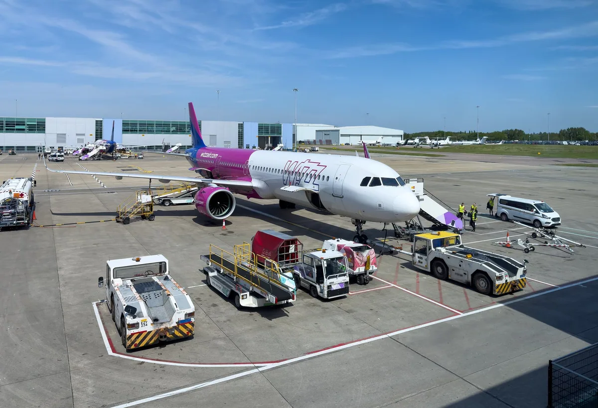 Wizz Air-fly ved gaten på London Luton Airport, omgitt av bakkeutstyr og med terminalbygget bak
