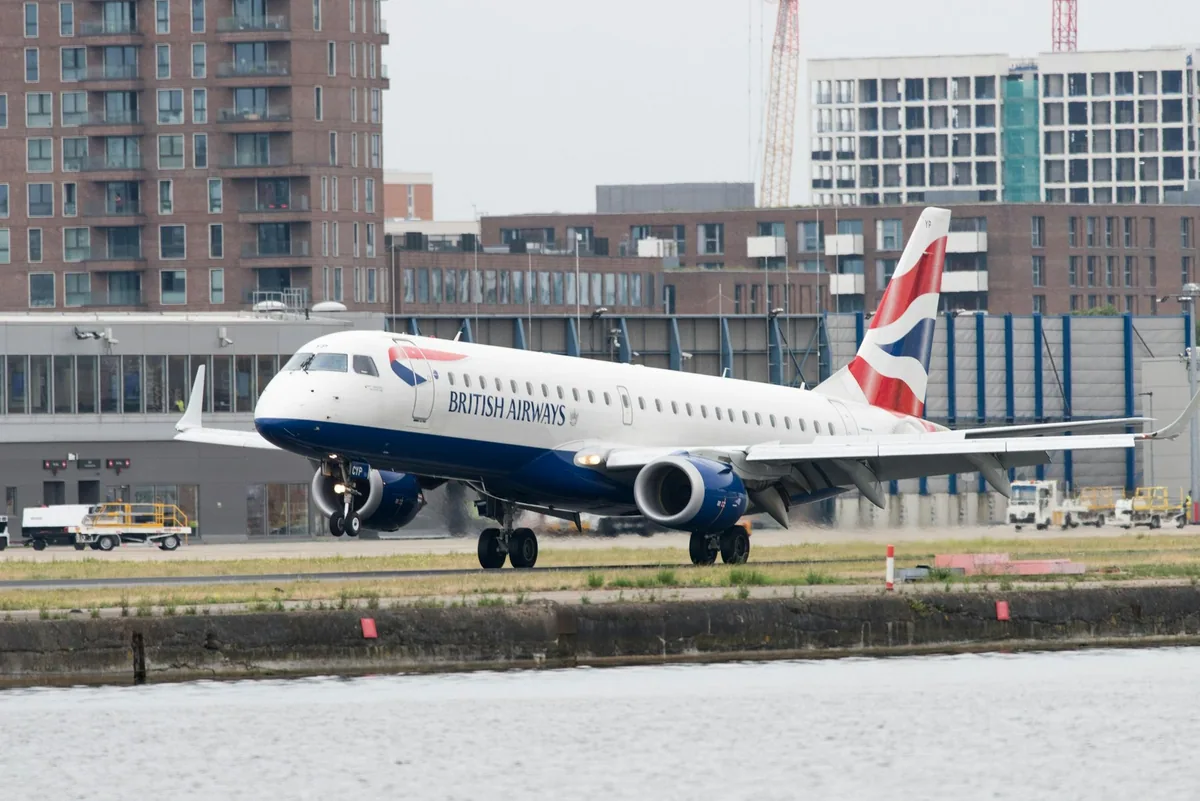 British Airways-fly på rullebanen ved London City Airport, sett over vannet i dokken foran