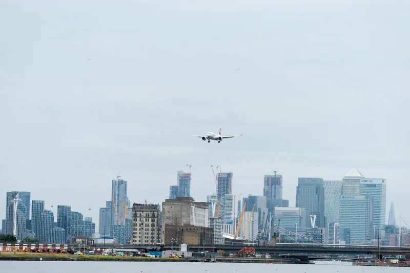 Passasjerfly på innflyging over dokkene mot London City Airport, med skyskraperne i Canary Wharf bak