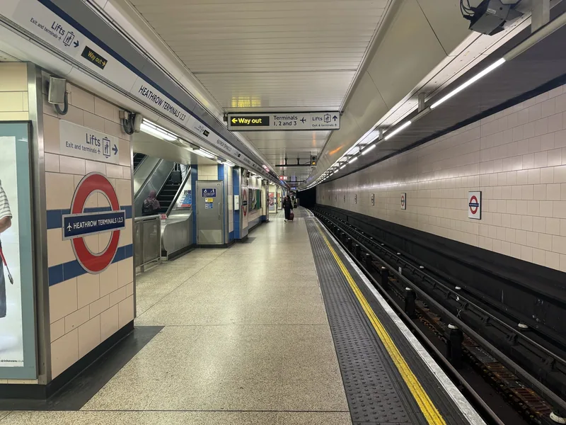 Nesten tom Piccadilly line-plattform på Heathrow Terminals 1, 2, 3 med skilt mot terminalene og heiser