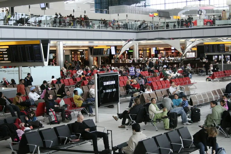 Reisende som venter på stoler i avgangshallen på Heathrow, under tavler med avgangstider