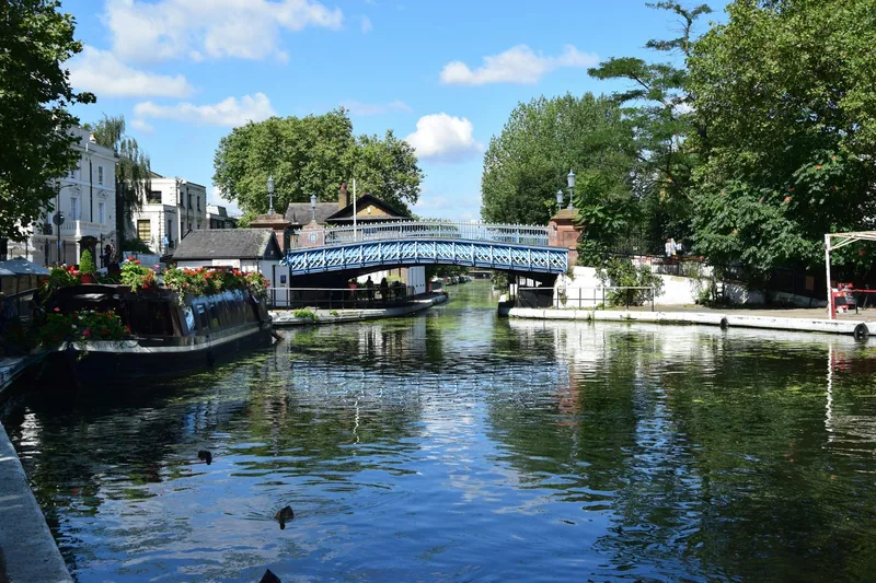 Kanalen i Little Venice en solrik sommerdag, med blå jernbro og en husbåt pyntet med blomster