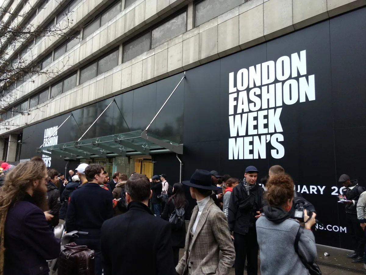 Folk og fotografer samlet foran 180 The Strand, dekket med store London Fashion Week Men's-skilt