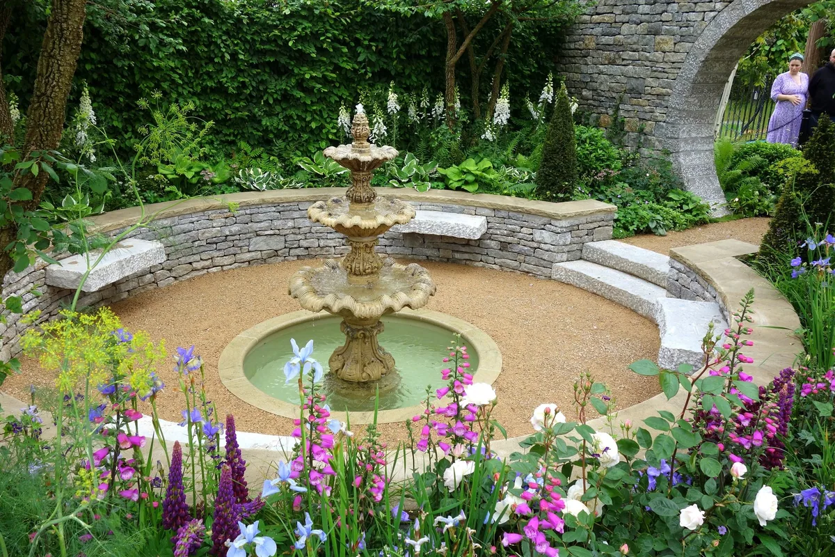 Visningshage på Chelsea Flower Show med fontene, steinbenker, revebjelle og roser