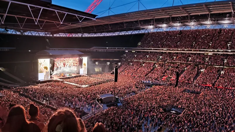 Fullsatt Wembley Stadium under en sommerkonsert, med scenen og storskjermene i den ene enden