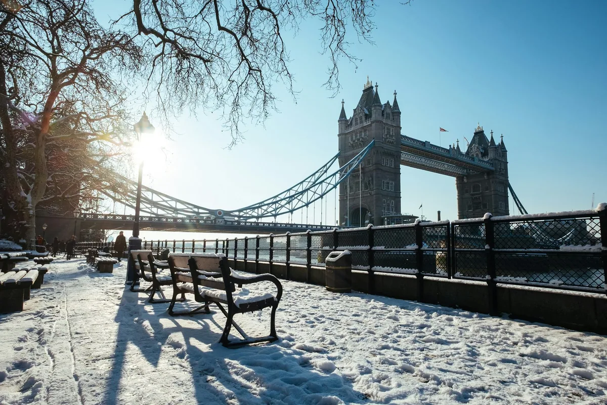 Tower Bridge i vintersol, sett fra en snødekt elvepromenade med benker og bare trær