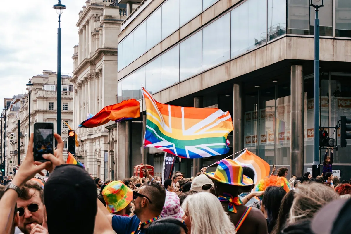 Regnbueflagg og et Union Jack i regnbuefarger over folkemengden under Pride-paraden i London