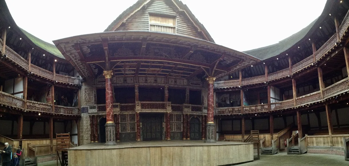 Scenen i Shakespeare's Globe med malte søyler og tak, omgitt av gallerier i eik under åpen himmel