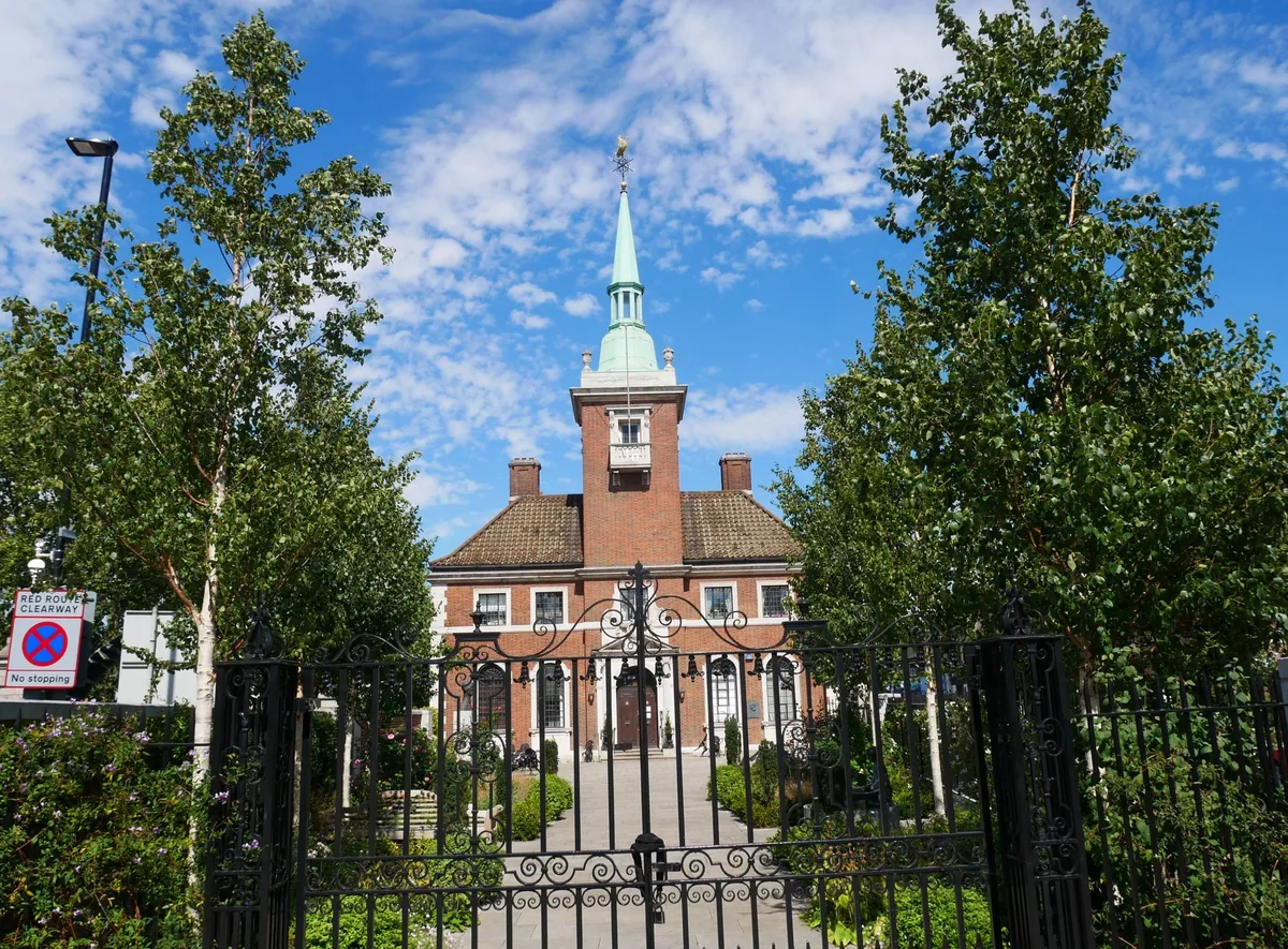 Den norske kirken St. Olav i Rotherhithe med rødt murverk og grønt spir, sett gjennom smijernsporten