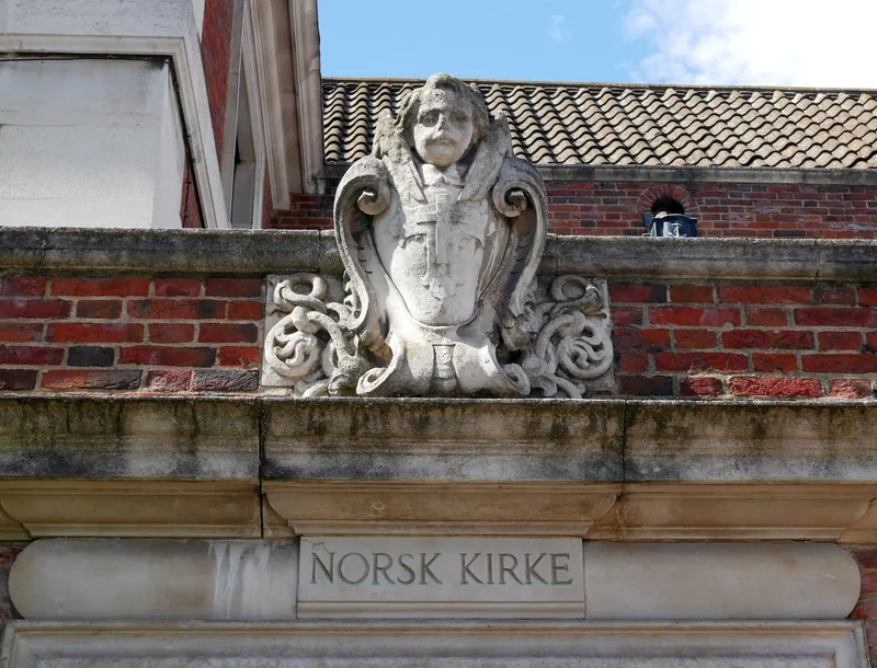 Innskriften NORSK KIRKE i stein under et utskåret våpenskjold på kirkens fasade