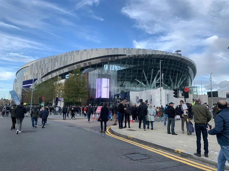 Tottenham Hotspur Stadium sett fra gaten, med folk på vei mot inngangene under blå himmel