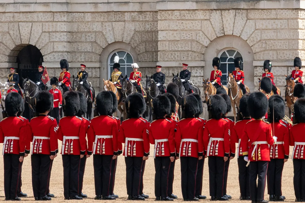 Gardesoldater i rød uniform og bjørneskinnslue foran ridende offiserer på Horse Guards Parade