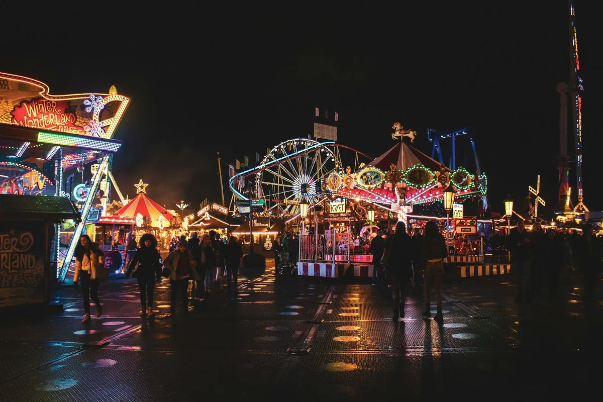 Opplyste boder, pariserhjul og karusell på Winter Wonderland i Hyde Park en kveld, med besøkende på den våte plassen