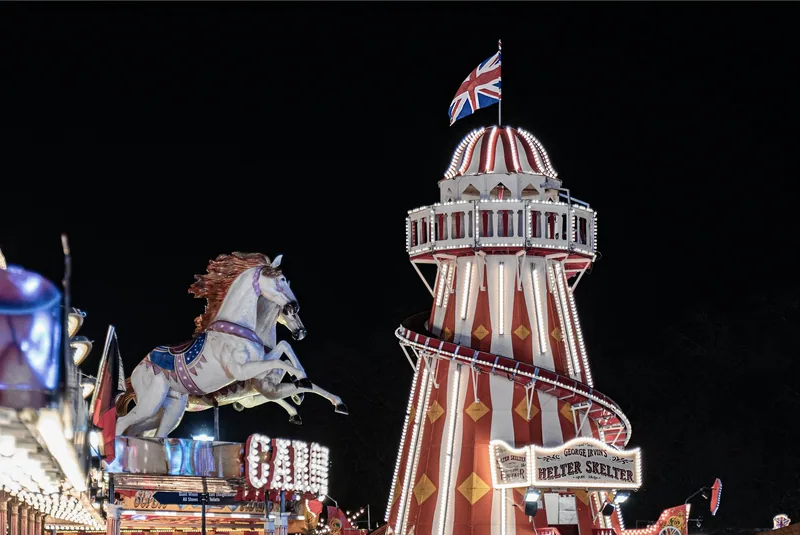Rødstripet helter skelter-sklie med britisk flagg på toppen og en karusellhest i lys på Winter Wonderland