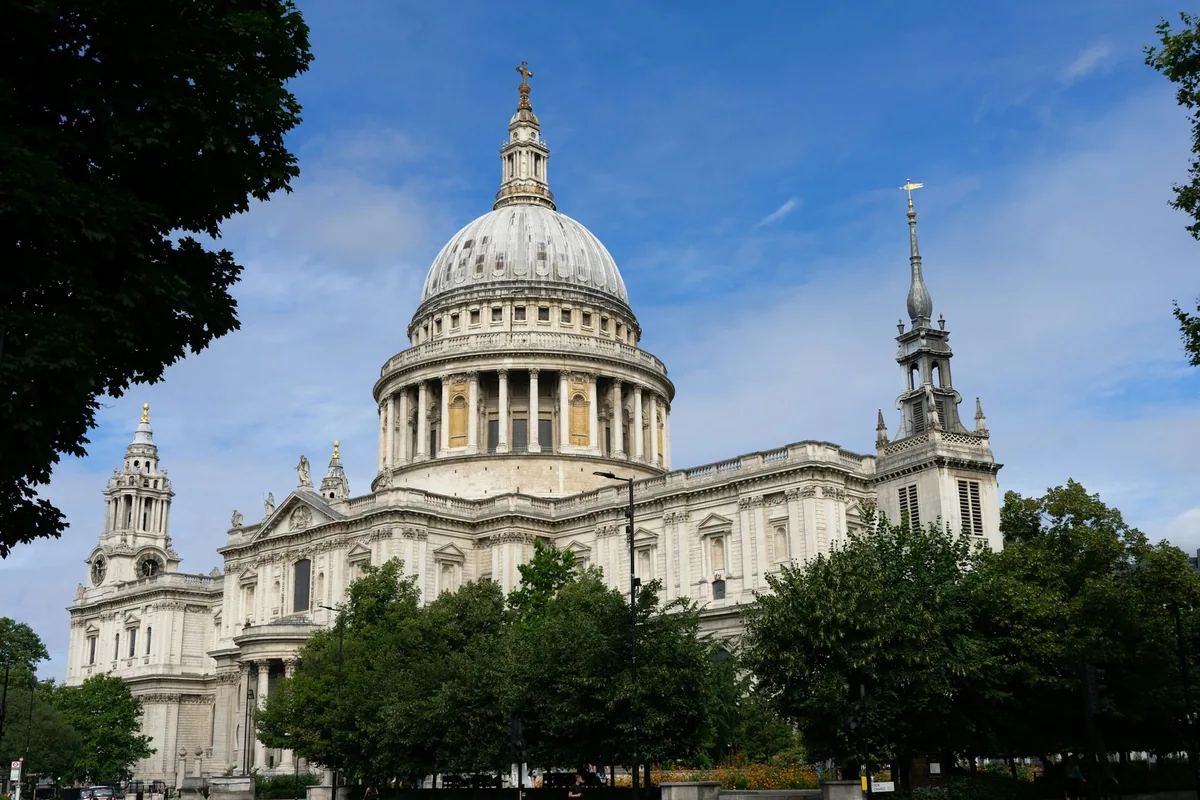 St Paul's Cathedral med den store kuppelen under blå himmel, med grønne trær foran