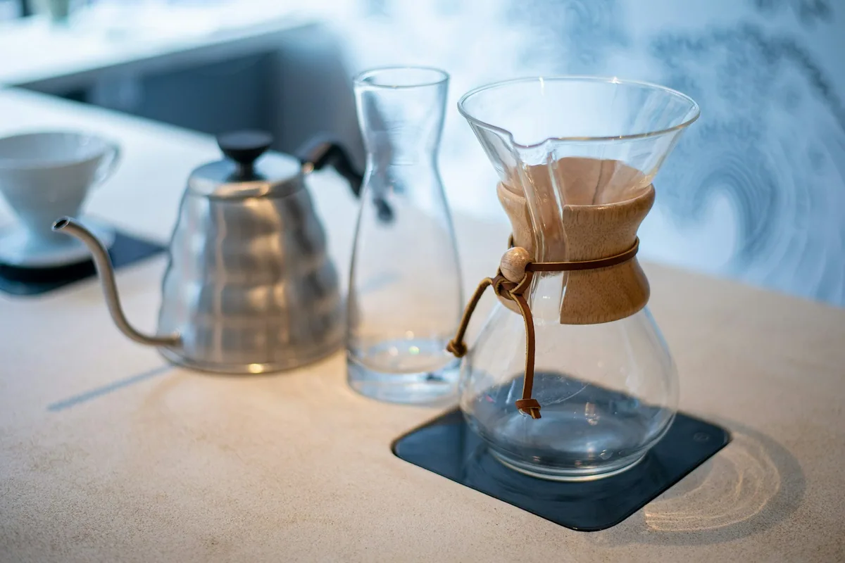 Chemex-kanne, glasskaraffel og vannkoker med svanehals klar til filterbrygging på en lys kafédisk