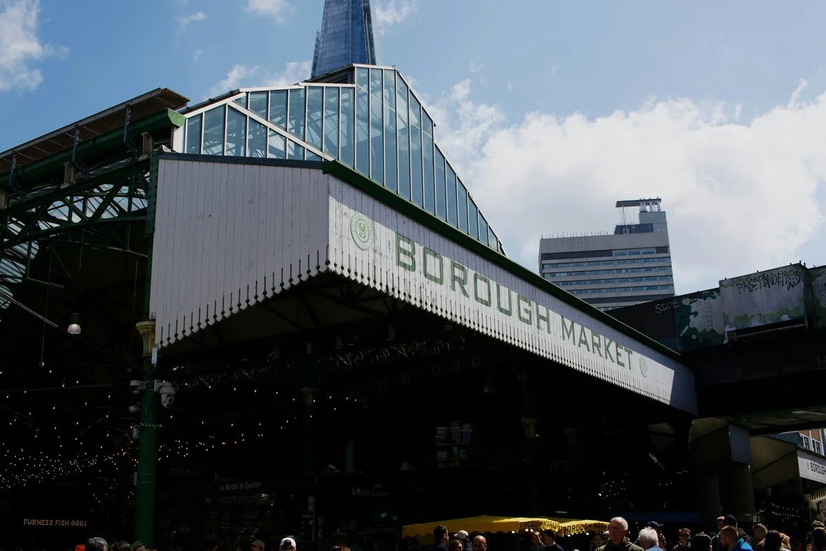 Det hvite Borough Market-skiltet på markedshallen med jernkonstruksjonen under og en kontorblokk mot skyene bak